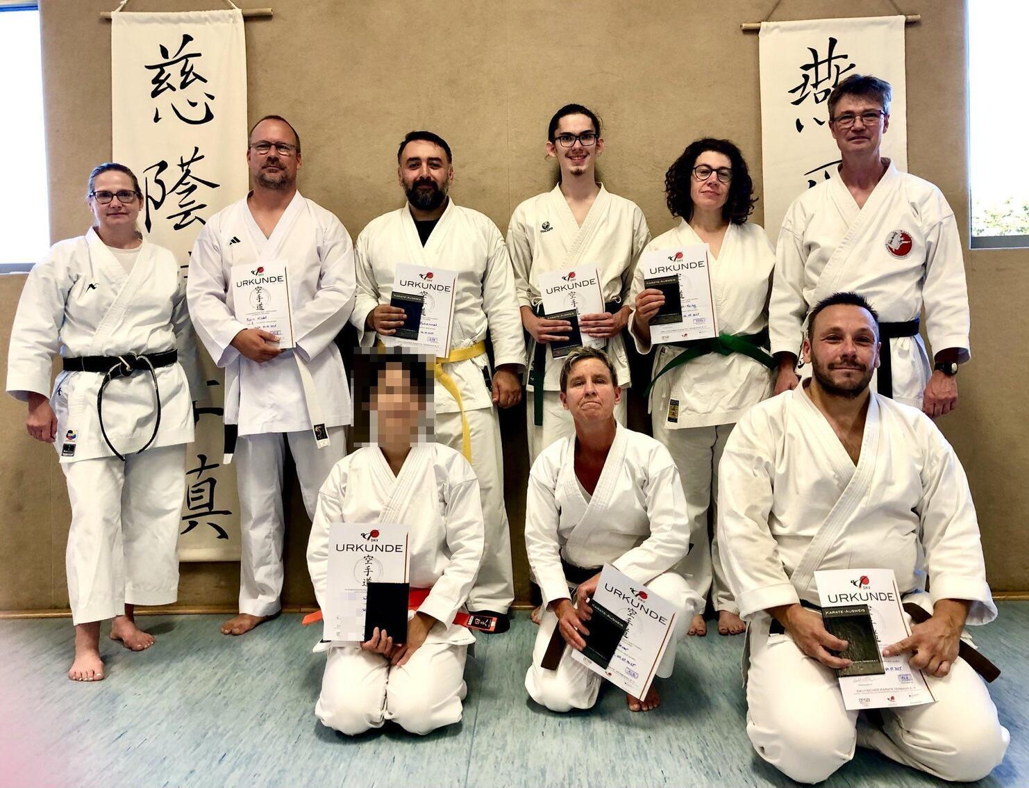 Gruppe von Karateka in Gi, halten Urkunden in einer Sporthalle vor einer Wand mit asiatischer Schrift.