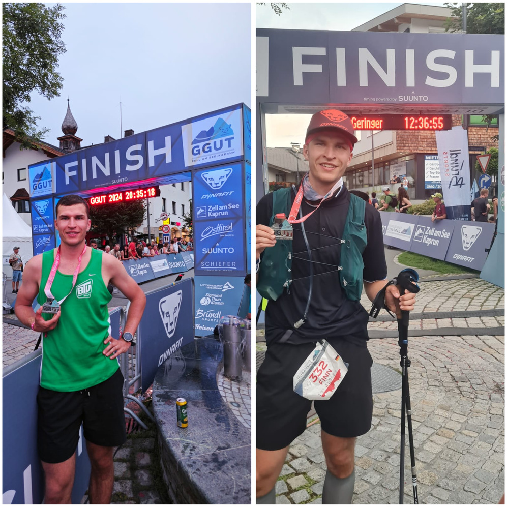 Zwei Läufer stehen am Zielbogen eines Rennens, jeder mit Medaille und unterschiedlichen Outfit.