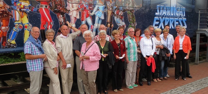 Gruppe älterer Personen posiert vor einem bunten Wandgemälde mit Motiven aus "Starlight Express".
