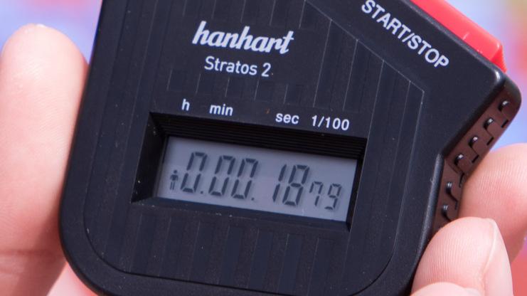Hand mit Stoppuhr "hanhart Stratos 2", die eine Zeit von 0:00:18,79 anzeigt, vor unscharfem Hintergrund.