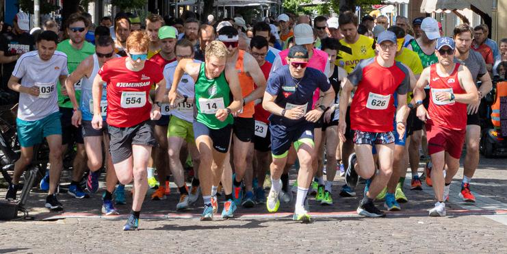 Startschuss für einen Lauf mit mehreren Teilnehmern in Sportbekleidung auf einem gepflasterten Weg.