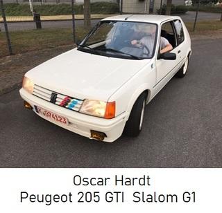 Weißer Peugeot 205 GTI fährt auf Straße, Fahrer sitzt am Steuer, Kennzeichen sichtbar.