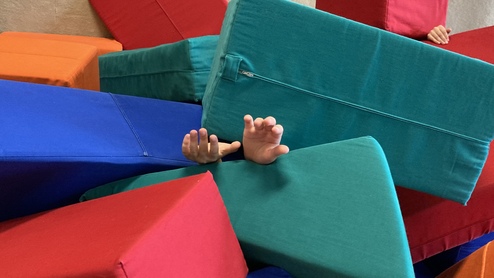 Bunte Schaumstoffblöcke in verschiedenen Farben, zwischen denen ausgestreckte Hände sichtbar sind.