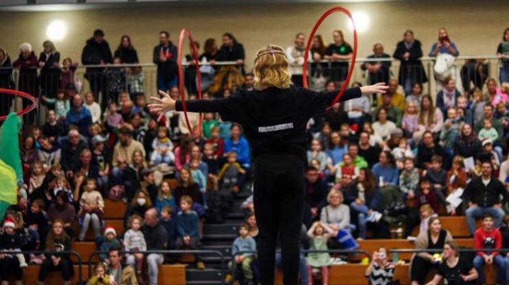 Akrobatin mit zwei Hula-Hoops steht im Mittelpunkt einer Bühne, umgeben von einem großen Publikum in einem Festsaal.