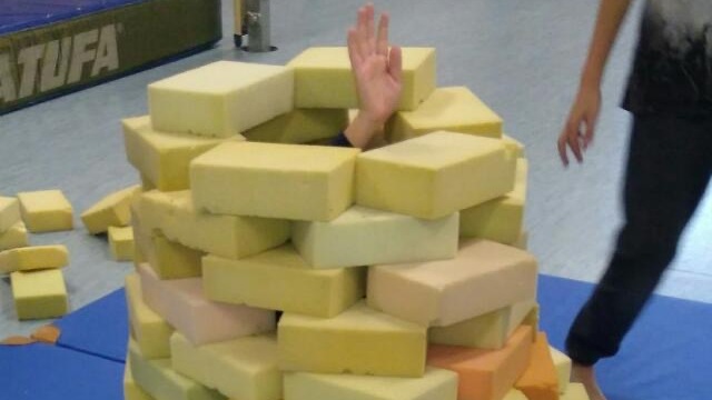 Hand, die aus einem bunten Haufen von Schaumstoffblöcken herausragt, mit einer Person im Hintergrund, die darauf zeigt.