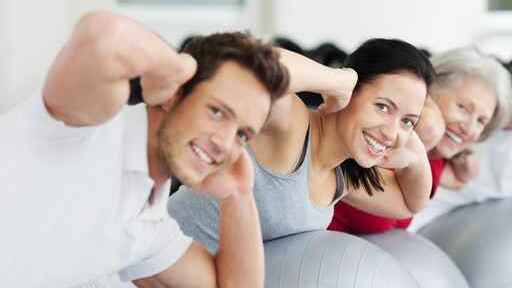 Vier Personen üben auf Gymnastikbällen, lächeln und zeigen mit ihren Händen an, dass sie stark sind.