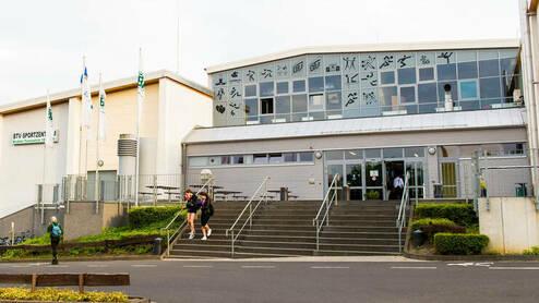 Eingang des BTN-Sportzentrums mit Treppe, Flaggen und mehreren Personen im Vordergrund.