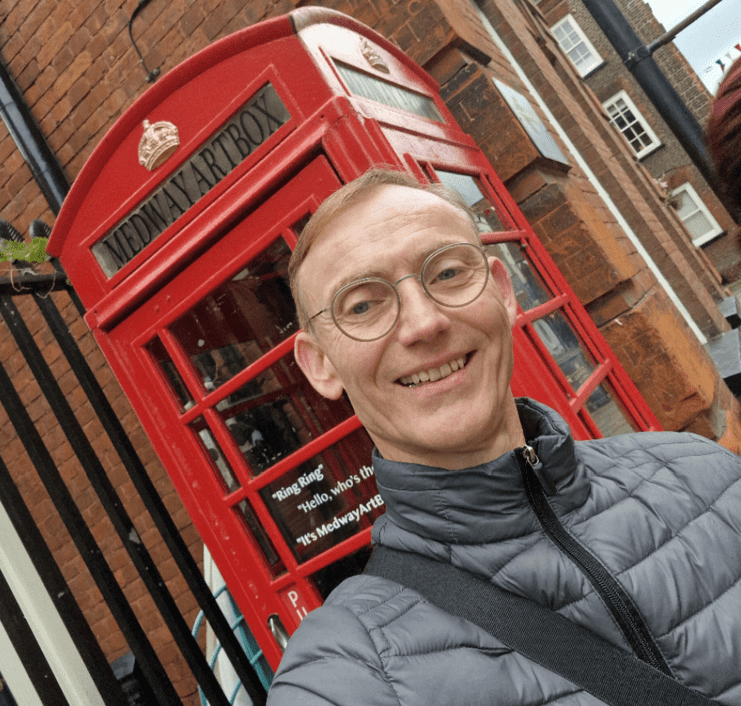 Mann in grauem Jackett lächelt vor einer roten Telefonzelle mit der Aufschrift „Medway Artbox“.