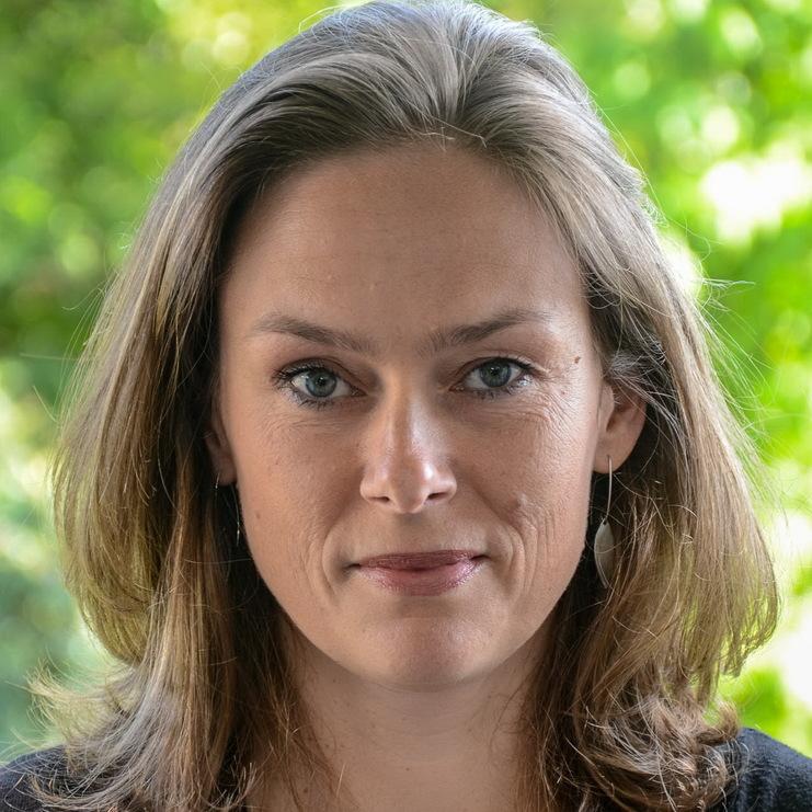 Porträt einer Frau mit langen, offen getragenen Haaren und Ohrhängern, vor unscharfem grünem Hintergrund.