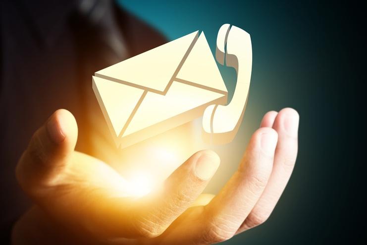 Hand eines Mannes hält ein leuchtendes Symbol für Brief und Telefon vor dunklem Hintergrund.