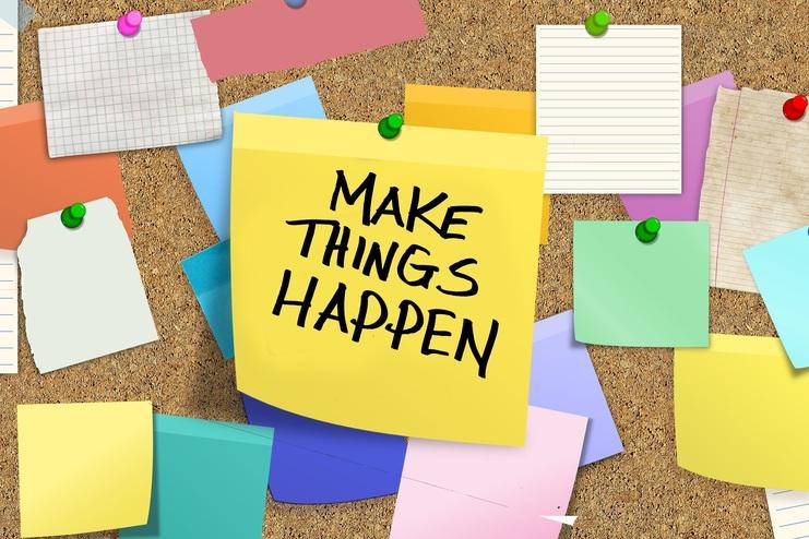 Bunte Haftnotizen und Zettel an einer Korkwand, mit einem gelben Zettel, auf dem steht: "MAKE THINGS HAPPEN".