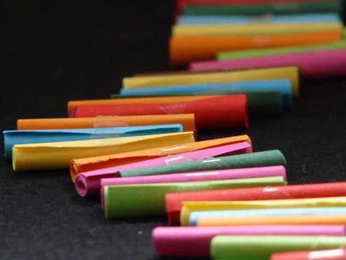 Bunte, gerollte Papierstreifen liegen in einem geschwungenen Muster auf schwarzem Hintergrund.