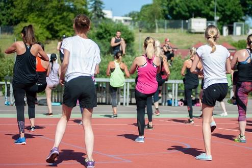 Gruppentraining im Freien: Frauen in Sportkleidung bewegen sich auf einer roten Laufbahn unter klarem Himmel.