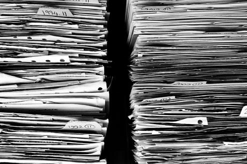 Zwei Stapel beschrifteter Papierunterlagen in Schwarz-Weiß, sortiert nach Jahr, angeordnet auf einem Tisch.