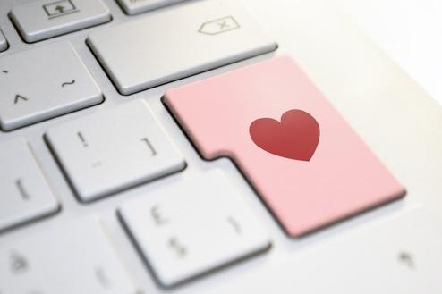 Tastatur mit rosa Taste, die ein Herzsymbol zeigt, im Vordergrund auf einem modernen Laptop.