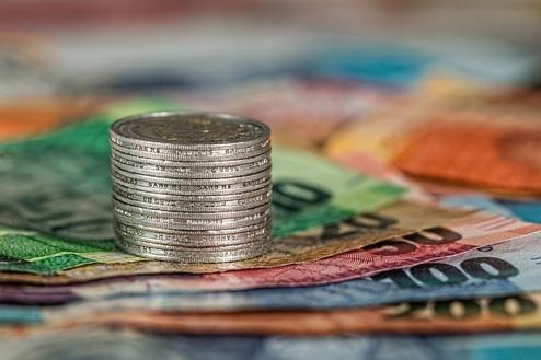 Ein Stapel von Münzen steht auf bunten Geldscheinen in unterschiedlichen Währungen, unscharf im Hintergrund.