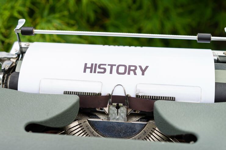 Nahaufnahme einer Schreibmaschine mit dem Wort „HISTORY“ auf einem weißen Blatt Papier.