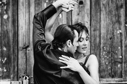 Tanzpaar in einem leidenschaftlichen Tango vor einer rustikalen Holztür, schwarz-weiß gehalten.