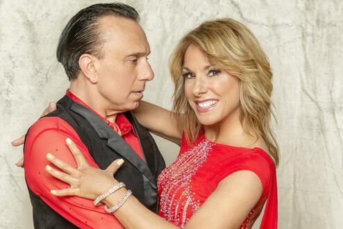 Tanzpaar in roten Kostümen posiert, der Mann hält die Frau in einer dynamischen Pose vor einem neutralen Hintergrund.