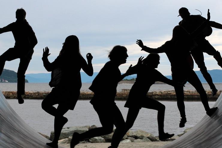 Silhouetten von sechs Personen in einer großen runden Struktur, die sich über einer Wasserfläche bewegen.