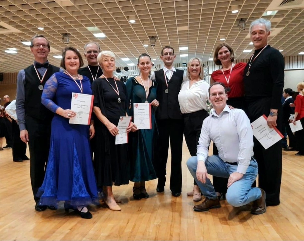 Gruppe von Tänzern mit Medaillen und Urkunden auf einer Tanzveranstaltung in einem großen Saal.