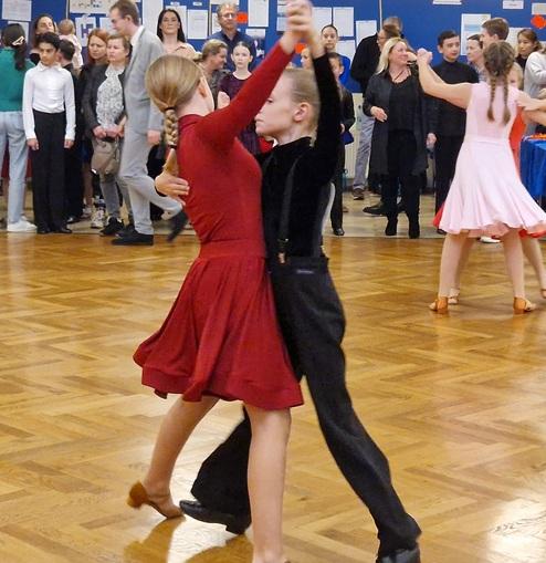 Tanzpaar in eleganter Kleidung tanzt, umgeben von Zuschauern in einem festlichen Saal mit Holzfußboden.