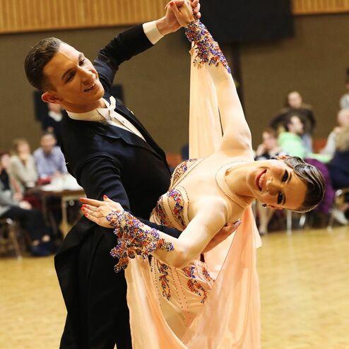 Tanzpaar in eleganter Pose auf der Tanzfläche, der Mann im Anzug, die Frau in glitzerndem Kleid.