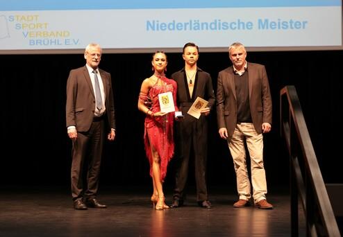Zwei Tänzer halten Urkunden und stehen mit zwei Männern auf einer Bühne bei der Preisverleihung der niederländischen Meisterschaften.