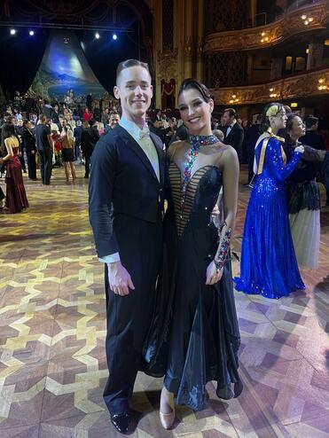 Ein tanzendes Paar in eleganter Abendkleidung posiert auf einer festlichen Tanzfläche mit Gästen im Hintergrund.