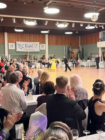 Tanzpaar in eleganter Kleidung beim Wettbewerb, umgeben von applaudierendem Publikum in festlicher Atmosphäre.