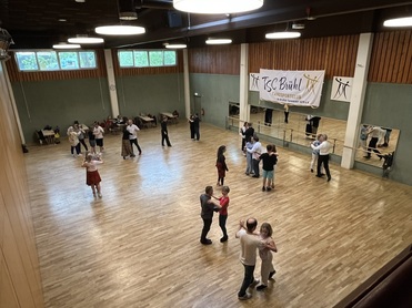 Tanzende Paare in einem großen Saal mit einem Banner des TSC Bühl und Spiegelwänden im Hintergrund.