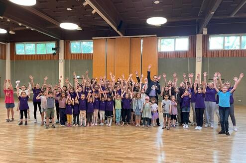 Gruppenszenen mit Kindern und Erwachsenen, die fröhlich die Hände heben, in einem großzügigen Veranstaltungsraum.