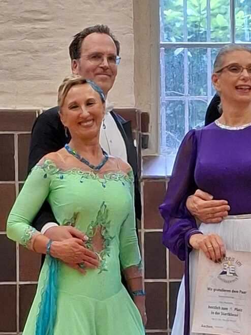 Tanzpaar in eleganter Kleidung, lächeln und halten eine Urkunde für den dritten Platz in der Startklasse.