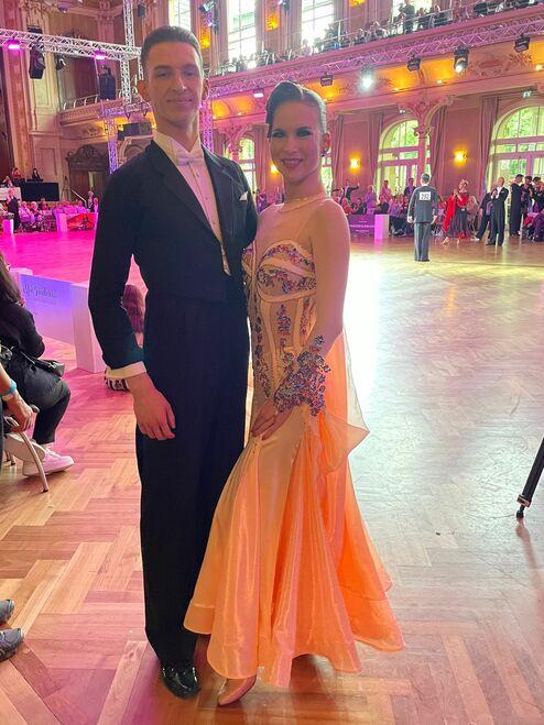 Tanzpaar in festlicher Kleidung posiert in einem festlich beleuchteten Saal während einer Tanzveranstaltung.