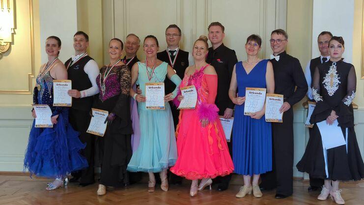 Gruppe von Tänzern in eleganter Kleidung, die Urkunden nach einem Wettbewerb in festlichem Raum halten.
