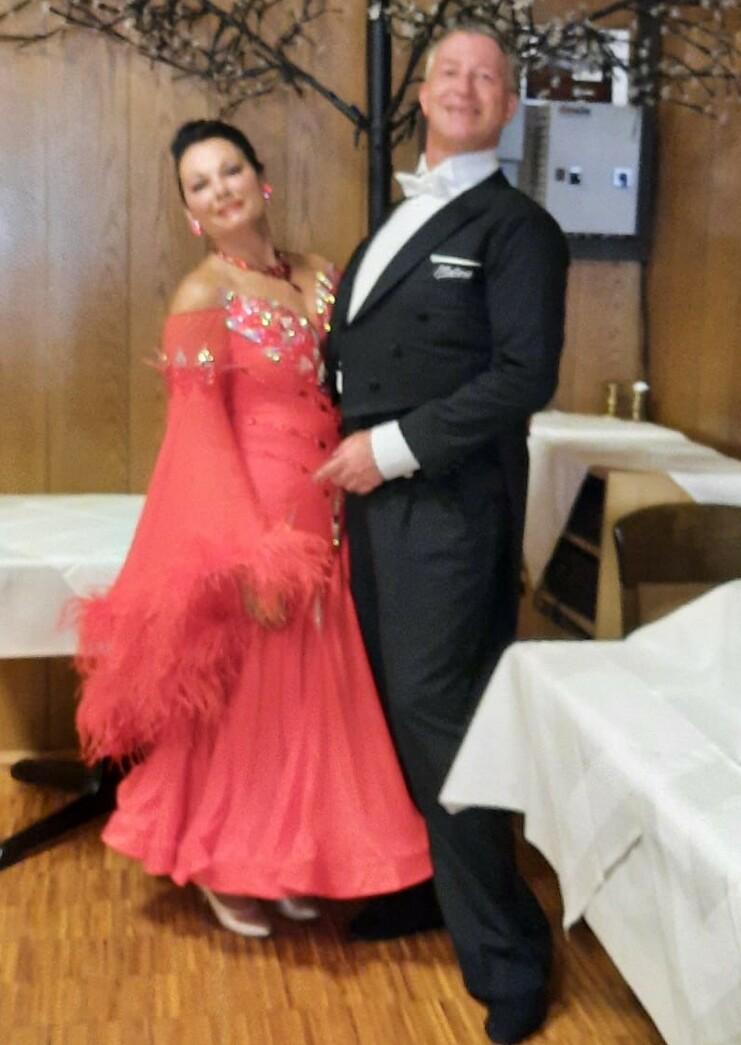 Tanzpaar in eleganter Kleidung, Frauenkleid in Koralle, lächeln im Innenraum vor Holzwänden und Dekoration.