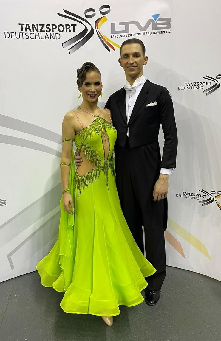 Tanzpaar in eleganter Kleidung, die Frau trägt ein leuchtend grünes Kleid, vor einem Tanzsport-Hintergrund.