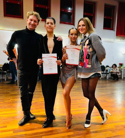 Zwei Jugendliche mit Urkunden für den 5. Platz stehen zusammen mit zwei Erwachsenen in einem Tanzsaal.