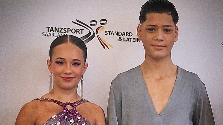 Zwei T&auml;nzer stehen mit einer Urkunde in der Hand vor einem Hintergrund mit Tanzsport-Logo.