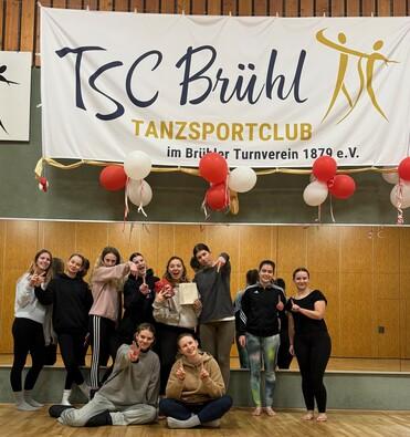 Gruppe von Tänzerinnen posiert vor einem Banner des TSC Brühl, dekoriert mit Luftballons, in einem Tanzsaal.