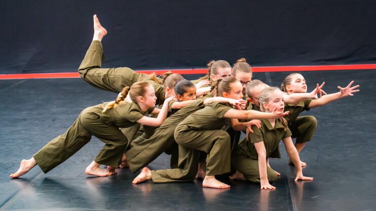 Gruppe junger Tänzerinnen in grünen Anzügen posiert dynamisch auf einer dunklen Tanzfläche.