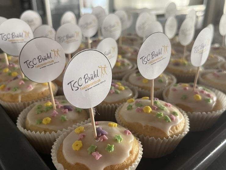 Verschiedene Muffins mit buntem Zuckerguss und kleinen TSC Brühl Aufstellern auf einem Blech.