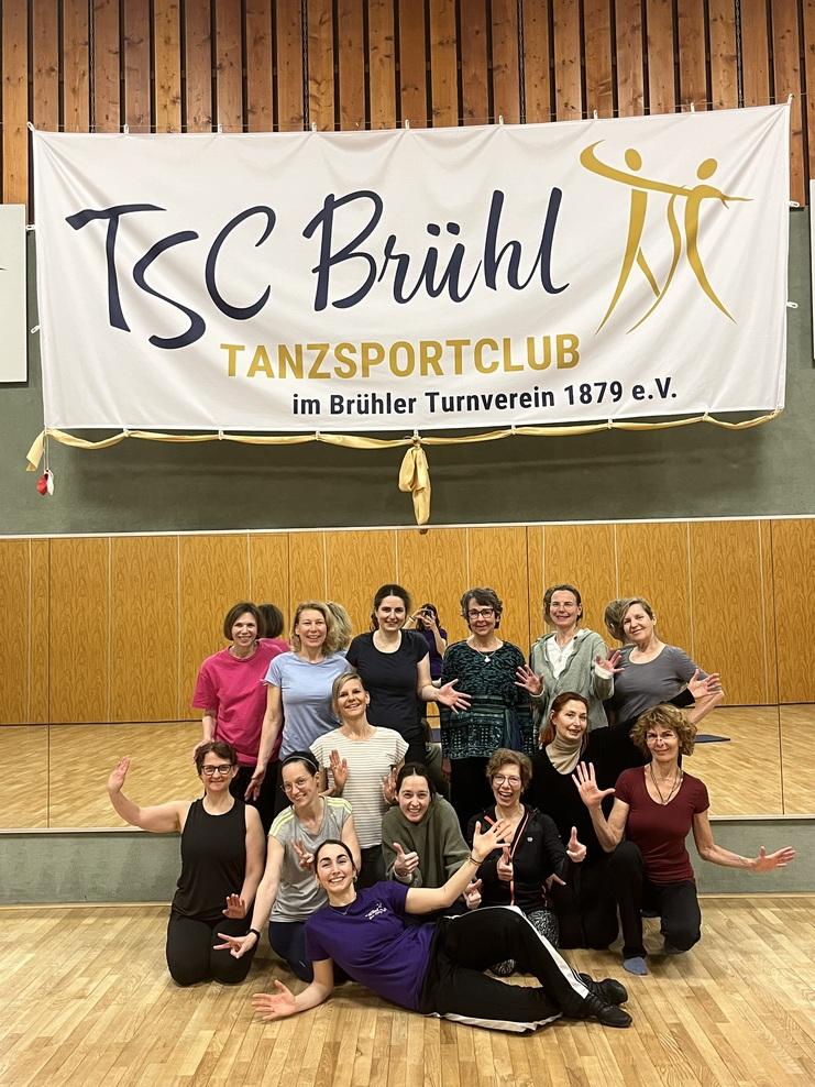 Gruppenzusammenkunft von tanzenden Frauen im TSC Brühl mit einem Banner des Tanzsportclubs im Hintergrund.