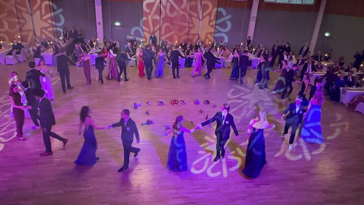 Tanzende Paare in eleganter Kleidung auf einer festlich beleuchteten Tanzfläche, umgeben von Gästen an Tischen.