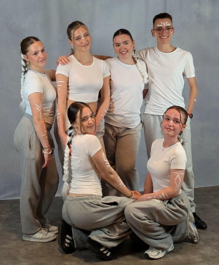 Sechs junge Menschen in heller Kleidung posieren in einem Studio, mit dekorativen Linien auf den Armen.