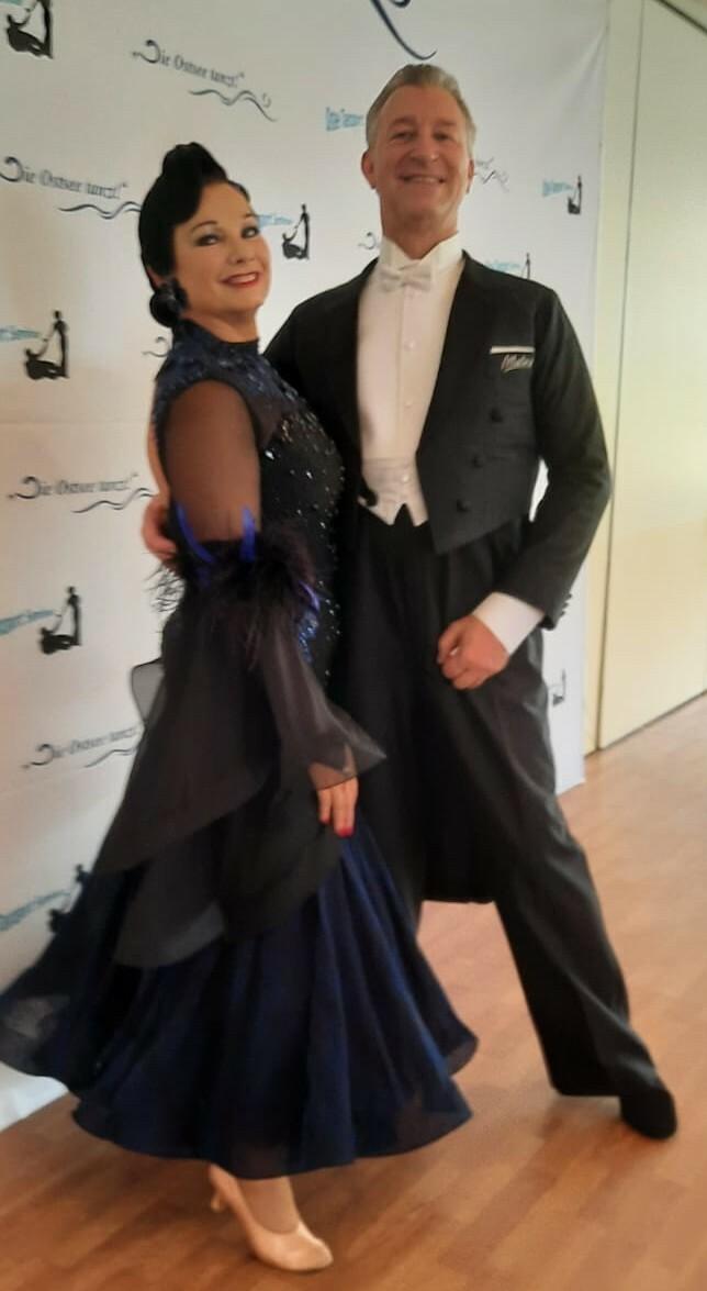 Tanzpaar in eleganter Abendkleidung, lächelnd vor einem weißen Banner mit dem Text „Die Osten tanzt“.