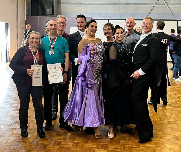 Gruppe von Tänzern mit Medaillen und Urkunden, lachend in festlicher Kleidung auf einem Tanzevent.