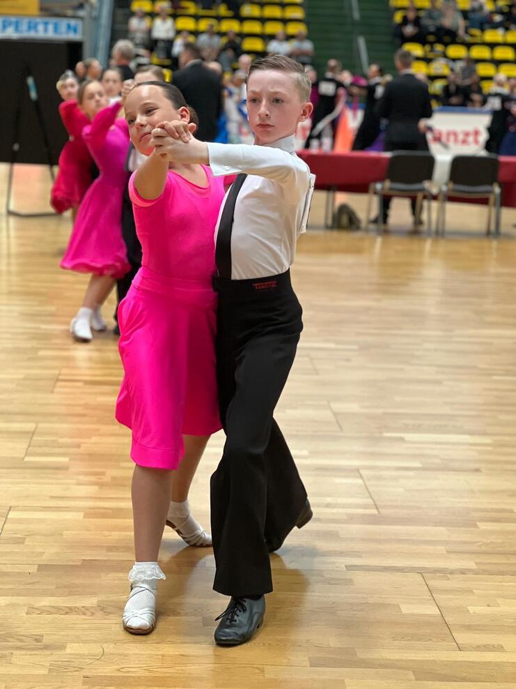 Tanzpaar in fröhlichen Kleidern führt einen Jugendtanz auf einer Holzfläche während eines Wettbewerbs.