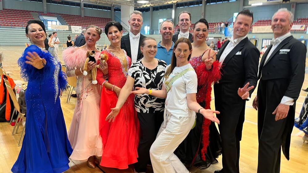 Gruppe von Tänzern in farbenfrohen Kostümen posiert fröhlich in einer Sporthalle.