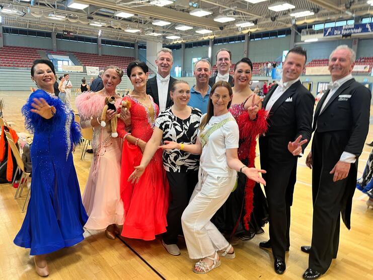 Gruppe von Tänzern in farbenfrohen Kostümen posiert fröhlich in einer Sporthalle.
